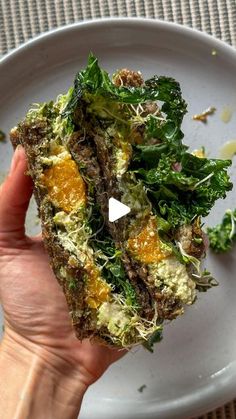 a white plate topped with greens and oranges next to a hand holding a piece of food