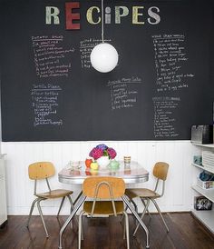 a kitchen table with chairs and a chalkboard on the wall behind it that says recipes