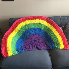 a crocheted rainbow rug sitting on top of a blue couch next to a pillow