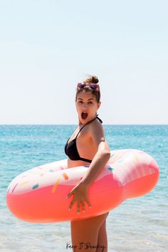 a woman in a bathing suit holding an inflatable donut on the beach