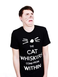 a man wearing a black t - shirt with the words, the cat whiskers come from within