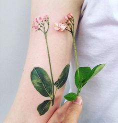 a woman's arm with pink flowers and green leaves on the left side of her arm