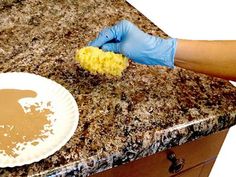 a person in blue gloves is cleaning a white plate on a granite counter top with a yellow sponge