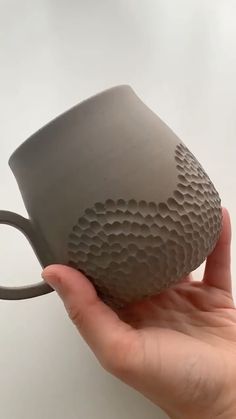 a hand holding a gray coffee mug with holes in it