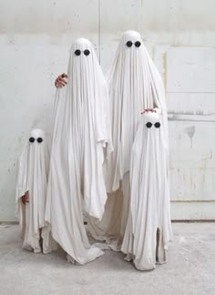 three white ghost statues standing next to each other with black eyes on their faces and arms