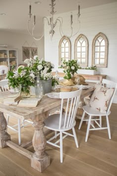 a dining room table with white chairs and flowers on it