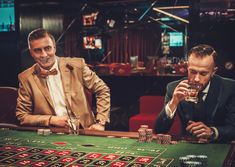 two men sitting at a casino table drinking beer and playing roulejack - stock photo - images