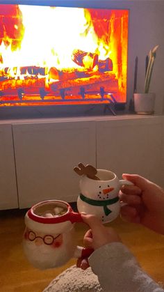 two people holding mugs in front of a fire place with christmas decorations on it