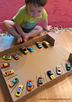 a toddler playing with toy cars on the floor in front of a cardboard box