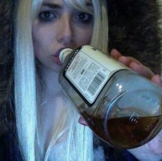 a blonde woman with long hair drinking from a bottle while wearing a fur coat on top of her head