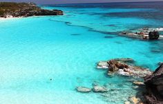 the water is crystal blue and there are people swimming in it on the rocks near the beach