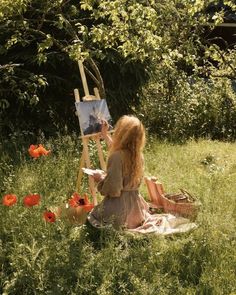 a woman sitting in the grass with an easel and paint on her lap next to some poppies