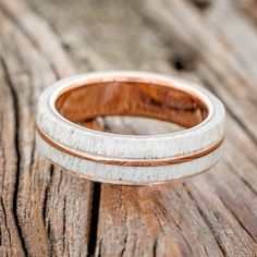 two wedding bands are sitting on top of a piece of wood, one is white and the other is rose gold