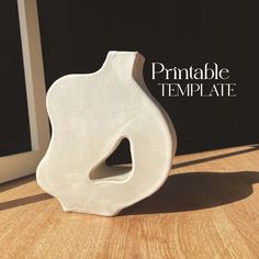 a white vase sitting on top of a wooden table next to a window sill