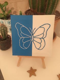 a blue and white card with a butterfly drawn on it next to potted cacti