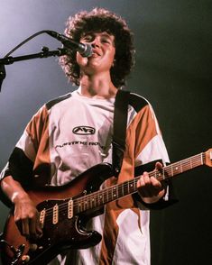 a young man holding a guitar and singing into a microphone