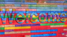 a colorful welcome sign painted on the side of a building with multicolored bricks