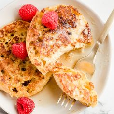 pancakes with raspberries and butter on a white plate next to a knife and fork