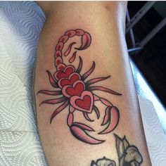 a scorpion tattoo with hearts on its back and tail, sitting on a white surface