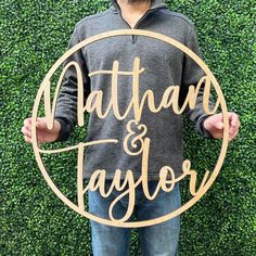 a man standing in front of a green wall holding a wooden sign that says nathan and taylor