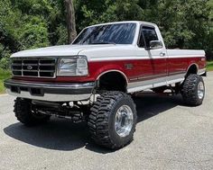 a red and white truck parked on top of a parking lot next to some trees