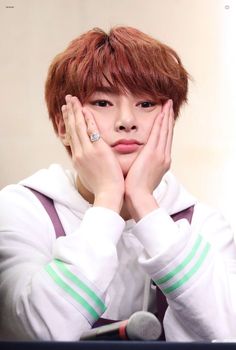 a young man with red hair holding his hands to his face while sitting in front of a microphone