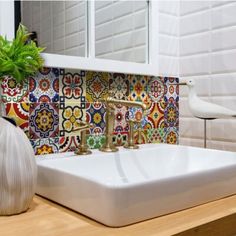 a white sink sitting under a bathroom mirror next to a vase with a green plant