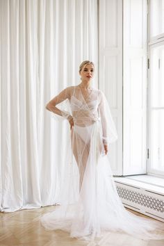 Elevate your wedding day preparations with the exquisite light ivory tulle bride robe with pearls and train, designed specifically for the bride's special morning. Designed in luxurious ivory tulle, this robe exudes grace and sophistication, giving it a timeless elegance. This robe, decorated with delicate pearls, shimmers with a subtle radiance, enhancing the beauty and charm of the bride. The soft, flowing fabric drapes elegantly, ensuring both comfort and style as the bride gets ready for her Pearl Bride, Flowing Fabric, Clothing Gifts, Light Ivory, Bridesmaid Outfit, Bridal Robes, Colored Wedding Dresses, Draped Fabric, Bridesmaids Gifts