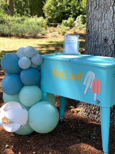 a blue piano with balloons on it in front of a tree and sign that says chill out