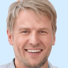 a man with blonde hair smiles at the camera while wearing a gray shirt and tie