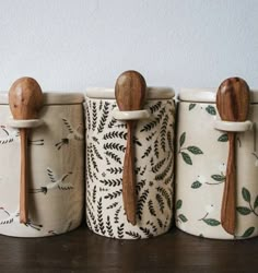 four wooden spoons are lined up next to each other in ceramic containers with designs on them