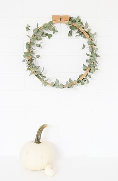 a white brick wall with a wooden wreath hanging on it's side and greenery in the middle