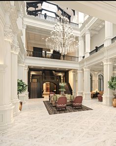 a large lobby with chandeliers and chairs in the center, surrounded by marble flooring