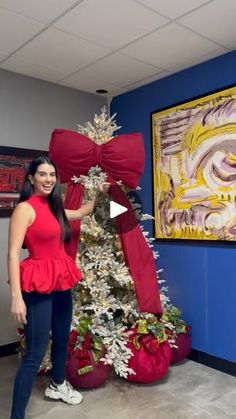 a woman standing next to a christmas tree in front of a painting on the wall