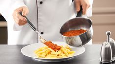 a person in a chef's coat is stirring pasta into a bowl with a ladle