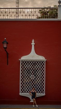 a woman walking past a red building with a white window and iron grilles on the side