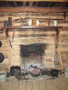 an old fashioned fireplace with pots and pans on the mantle in a log cabin