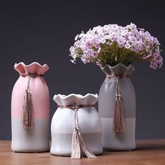 three vases with tasseled handles and flowers in them sitting on a table