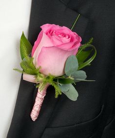 a pink rose boutonniere on a black suit lapel piece with green foliage