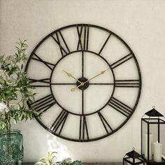 a large clock on the wall next to a potted plant and candle holder with flowers