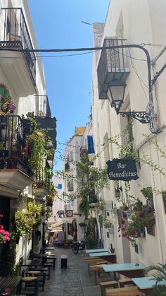 an alleyway with tables and chairs lined up against the wall, surrounded by plants