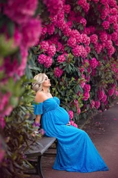 a pregnant woman in a blue dress sitting on a bench with pink flowers behind her