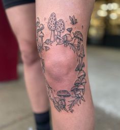 a tattoo on the leg of a woman with mushrooms and leaves around her legs,