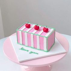 a pink and white cake with two cherries on top is sitting on a table