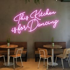 this kitchen is for dancing neon sign on the wall above two wooden tables and chairs