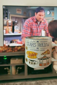 a person holding up a coffee mug in front of a flat screen tv with the star's hollow logo on it