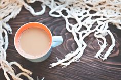 a cup of coffee sitting on top of a wooden table next to some white yarn