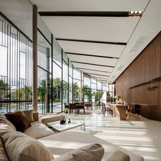 a large living room with couches and tables in front of glass walls that look out onto an outdoor swimming pool