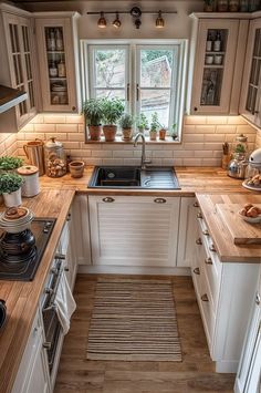 a kitchen with wooden counter tops and white cabinets, along with potted plants on the window sill