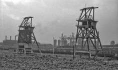 an old black and white photo of two industrial structures in front of a train yard